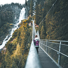 Besucher überquert eine Hängebrücke beim  Stuibenfall Wasserfall im Ötztal und erkundet Outdoor-Erlebnisse.